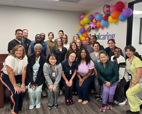 Diverse healthcare team celebrating at VitalCaring office with colorful balloons.