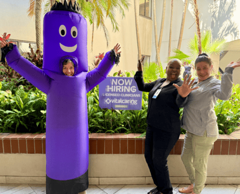 VitalCaring team celebrating at hiring event with mascot in outdoor setting.