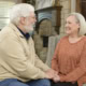 Elderly man and woman talking and smiling in a cozy living room.