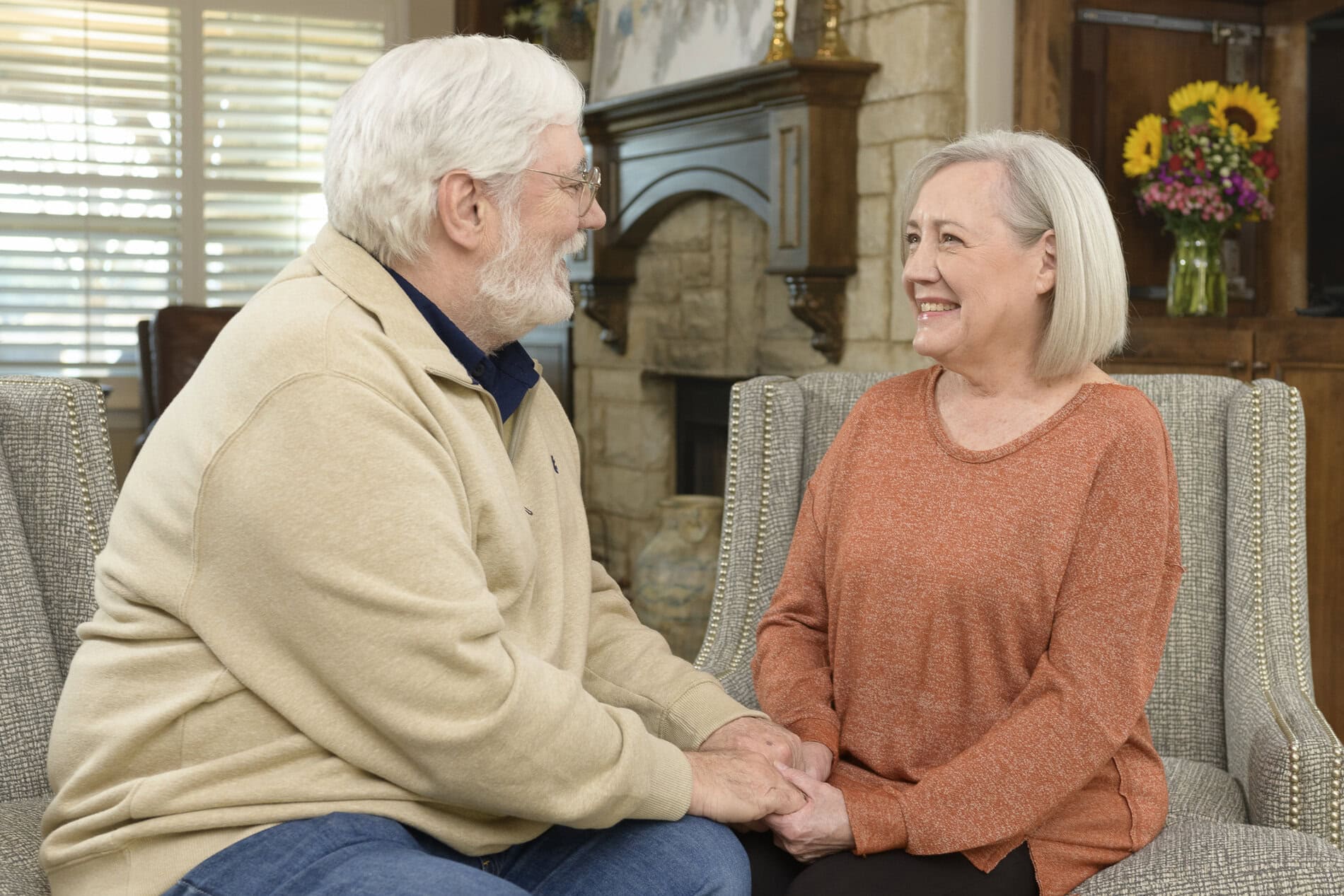 Elderly man and woman talking and smiling in a cozy living room.